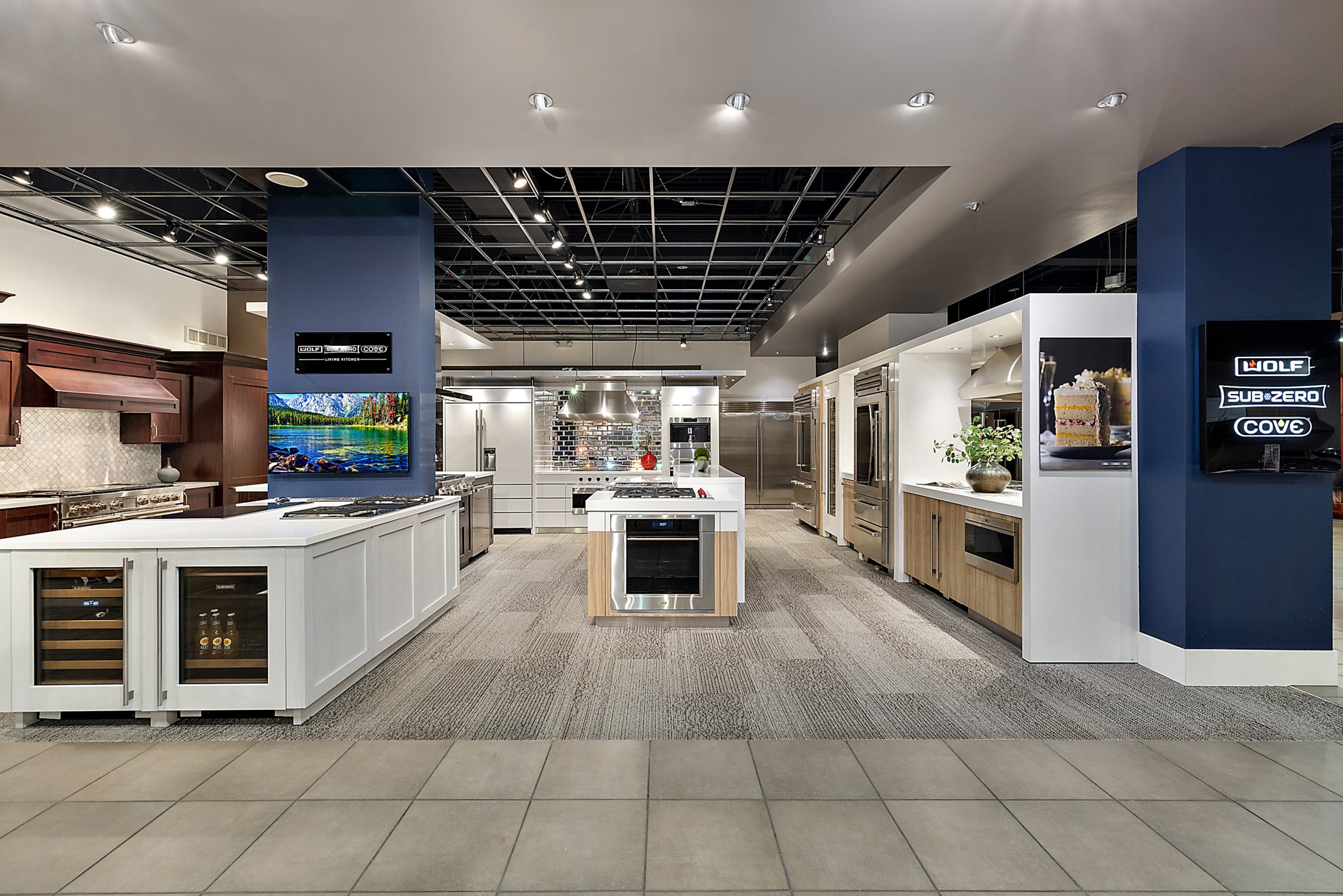 Wide view of appliance showroom with multiple kitchen setups and lighting